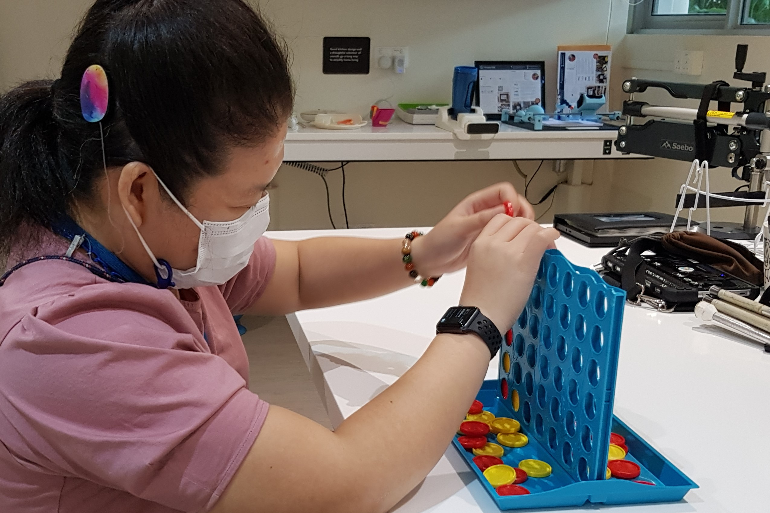 Siew Ling playing with the Connect Four game by dropping a tactile chip into a vertical slot.