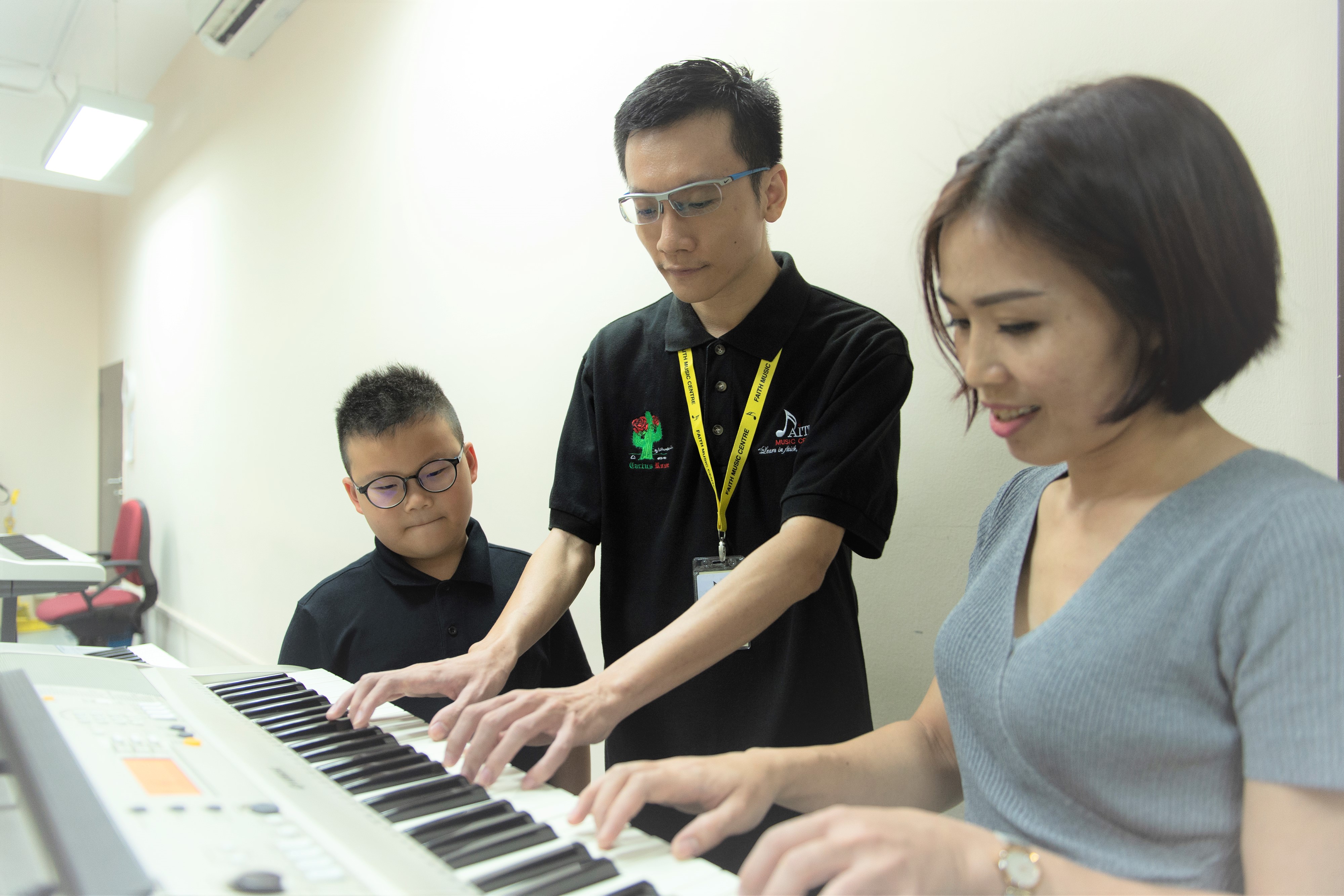 Two adults and a child playing the keyboard at Faith Music Centre
