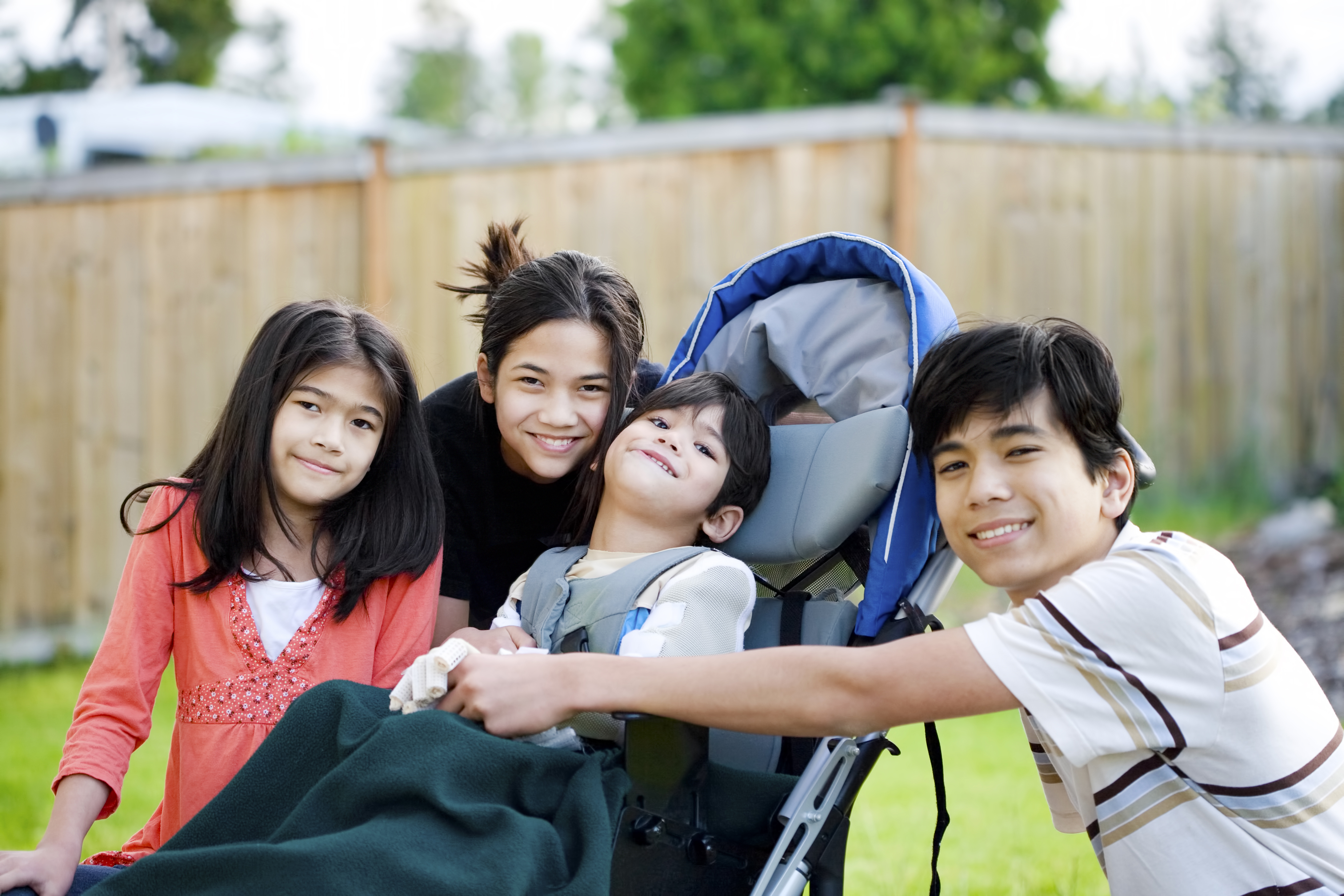 A stock photo showing a group of young caregivers with a young boy with disabilities in a pram.