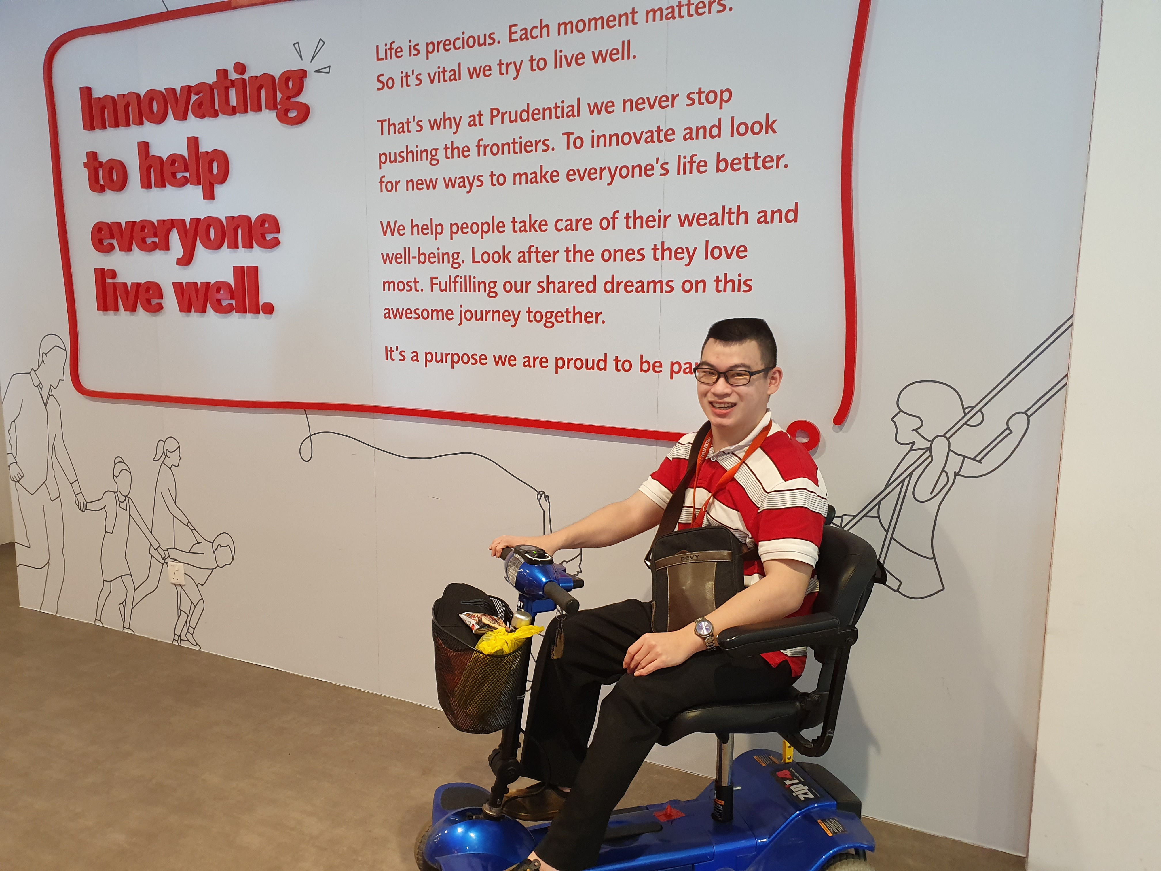 A bespectacled man on a motorised wheelchair in front of a Prudential-branded wall smiles for the camera.